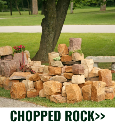 Stacked tan and orange chopped rock landscaping stones beside a tree in a yard, labeled “CHOPPED ROCK”