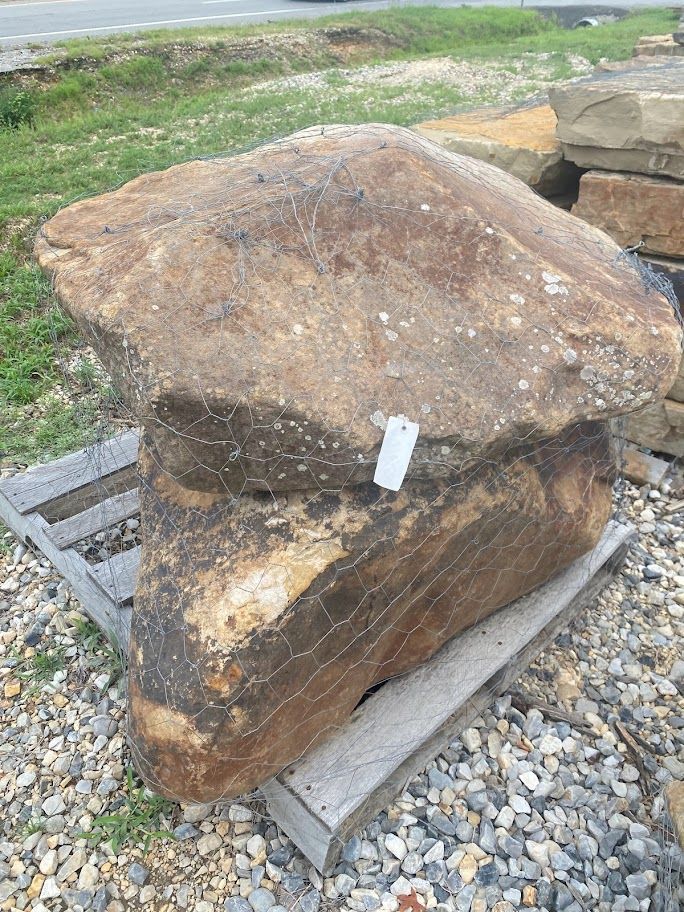 Large brown stone slab on a wooden pallet beside gravel and grass outdoors