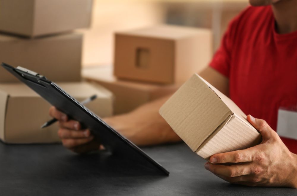 Person Packing a Cardboard Box Beside a Tablet at a Shipping Station — Access Couriers in Port Macquarie, NSW