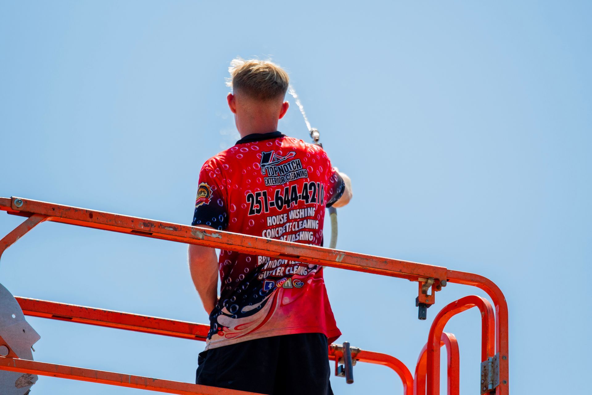 A man in a red shirt is standing on top of an orange ladder.