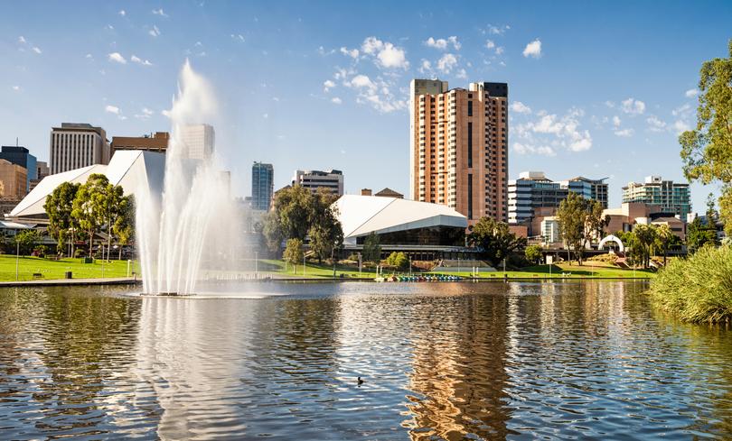 Fountain sprays in front of Adelaide skyline, featuring tall buildings and blue sky over the lake.