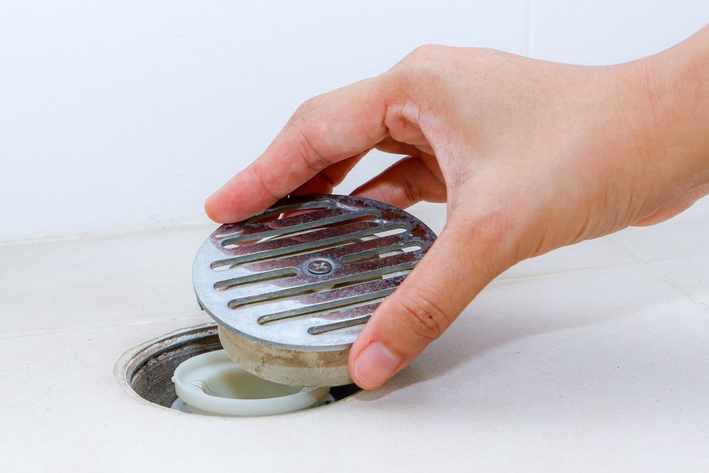 A person is cleaning a drain in a bathroom.