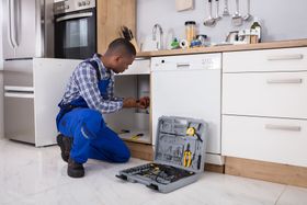 professional plumber repairing pipes under kitchen sink