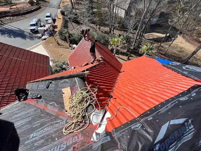 Construction worker in orange vest and blue helmet hammering on a rooftop.