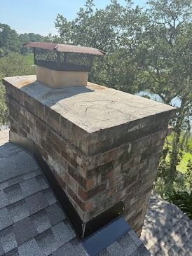 Brick chimney on a roof, topped with a metal mesh cap.