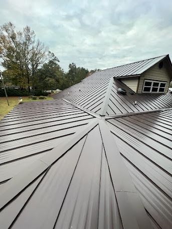 Brown metal roof with a dormer against a cloudy sky.