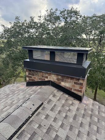 Chimney on a shingled roof with a dark metal cap and brick base.