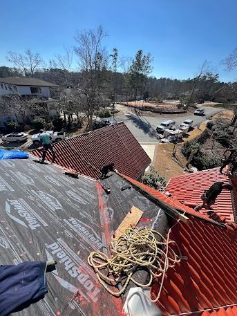 Roofers working on a red tile roof on a sunny day, with surrounding houses and trees in the background.