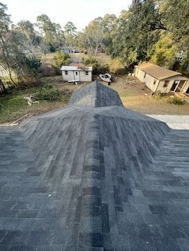 Newly shingled dark roof with a view of a rural setting including small homes and trees.