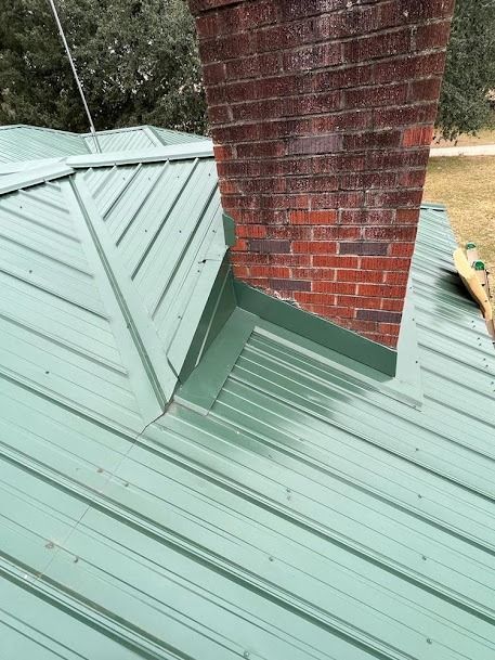 Green metal roof with brick chimney and flashing.
