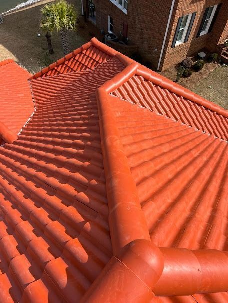 Red tiled roof with curved tiles and a downspout on a brick building.