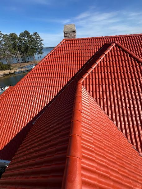 Red tile roof on a building, chimney, blue sky, trees and water in the background.