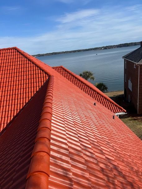 Red tile roof of a building overlooking a blue body of water under a blue sky.