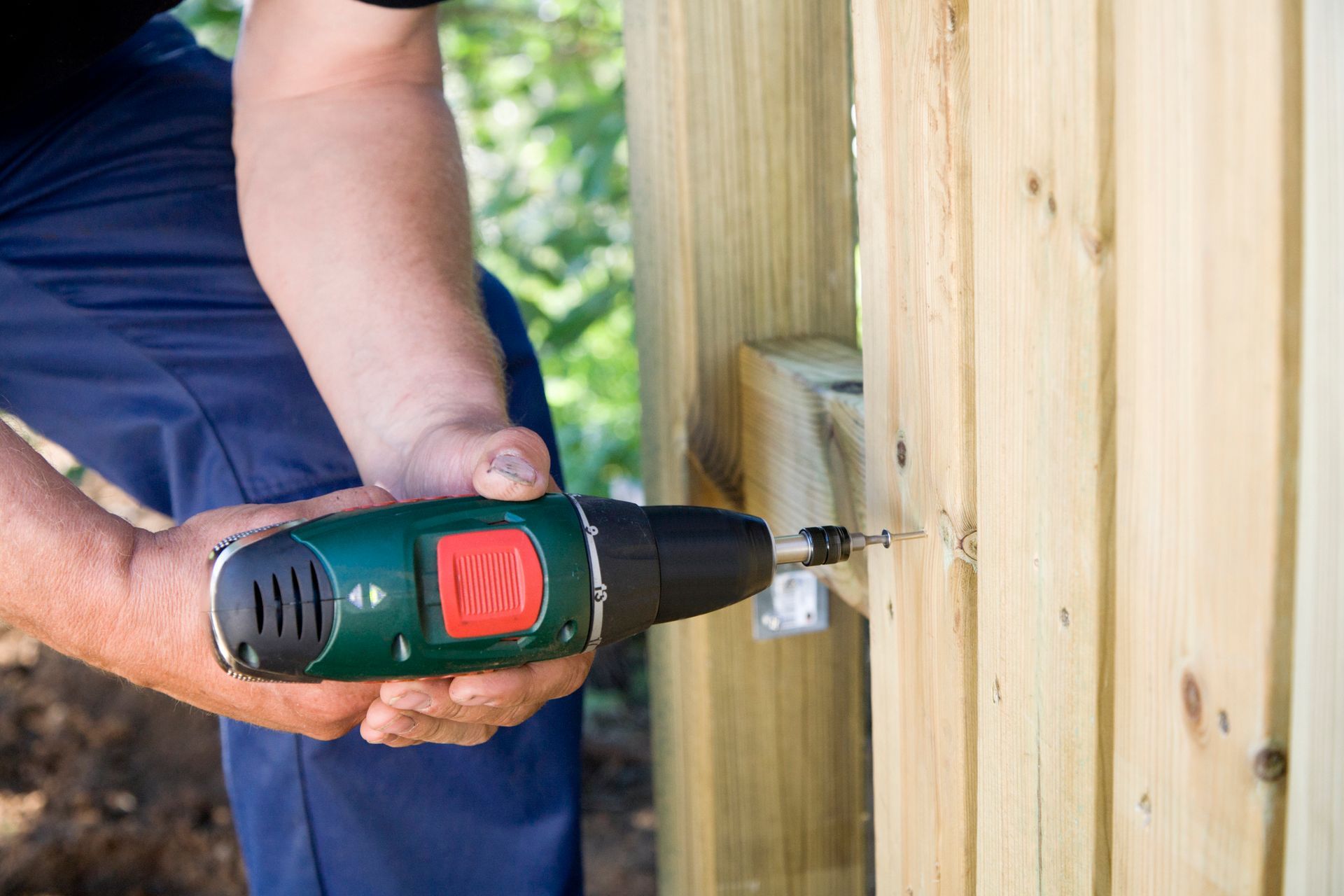Person using a cordless drill to screw into a wooden fence.
