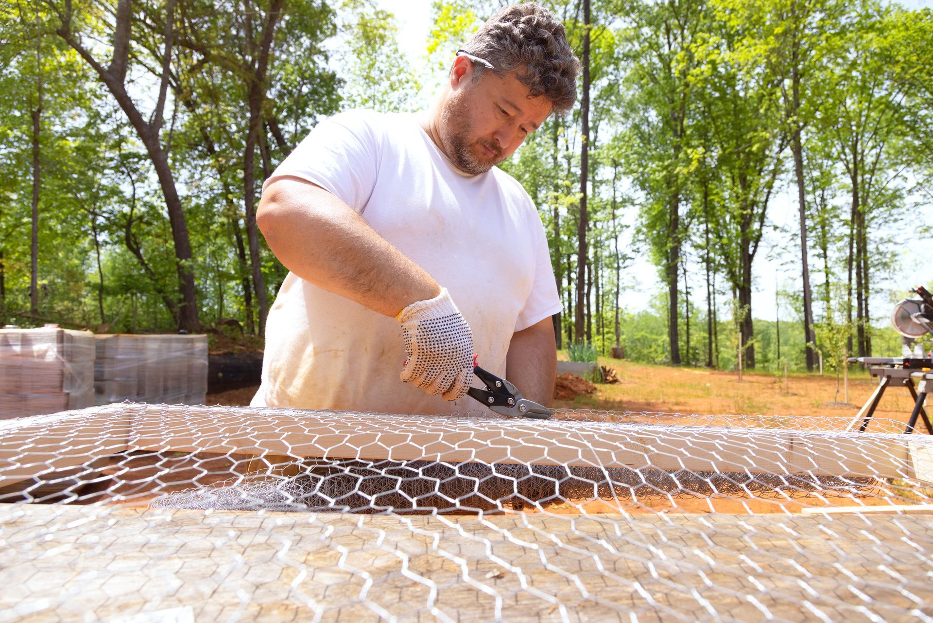 A worker cuts metal mesh using scissors for a chain-link fence installation. A worker cuts metal mesh using scissors for a chain-link fence installation.