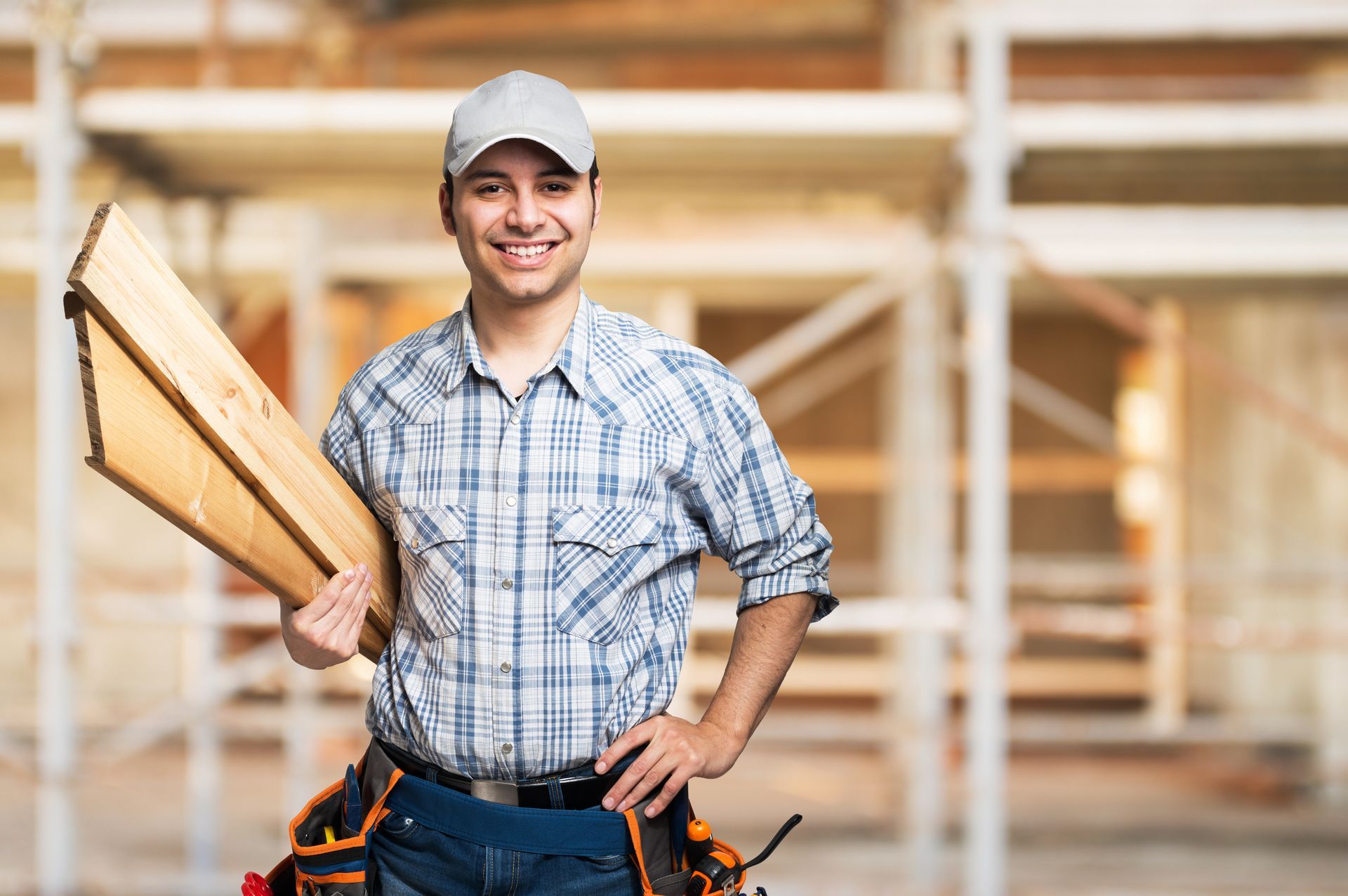 Construction worker holding wooden planks with tool belt at building site.