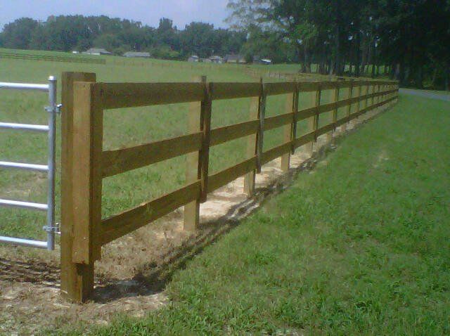 Wooden fence with metal gate in a grassy field.