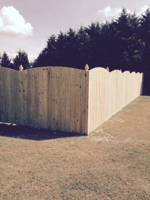 Wooden fence in a grassy yard, with trees in the background under a cloudy sky.