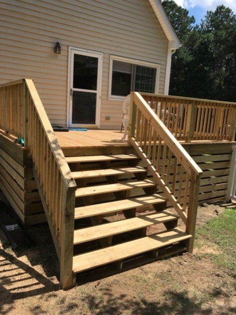 Wooden deck with stairs leading to a back door of a light-colored house on a sunny day.