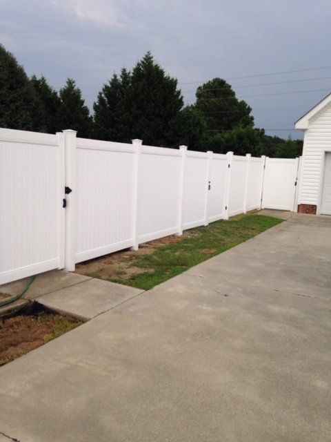 White vinyl fence encloses a backyard with a concrete driveway and grass.
