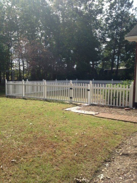 White picket fence encloses a backyard with trees, creating a defined property boundary.