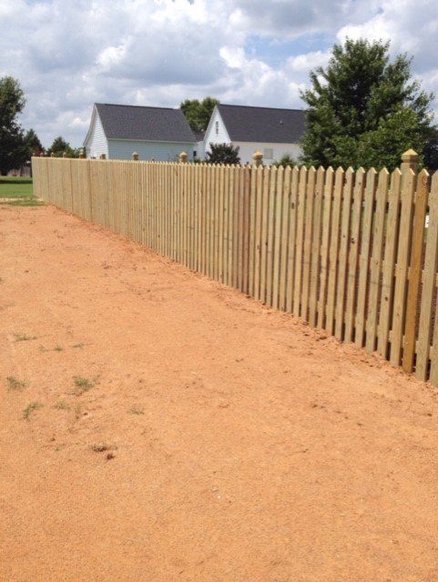 Wooden picket fence in a red dirt yard, with houses in the background.