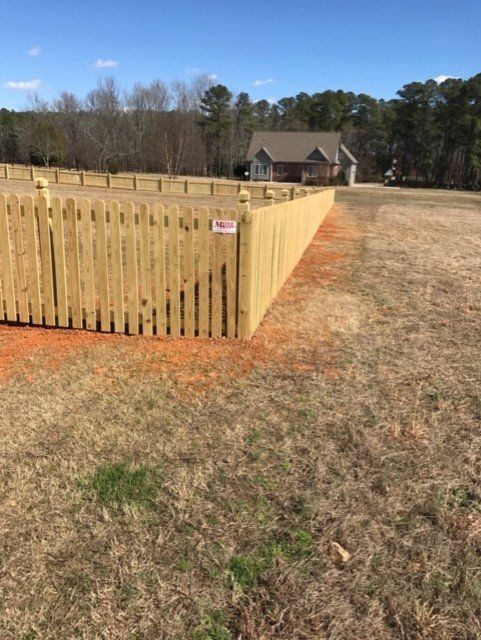 Wooden fence surrounds a yard in front of a house on a sunny day.