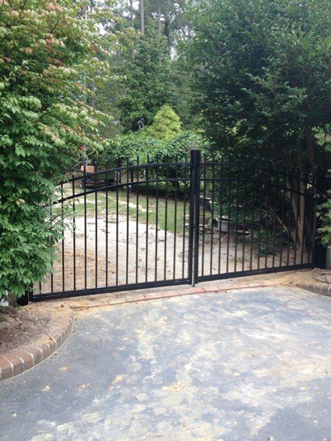 Black metal driveway gate in a yard with trees.