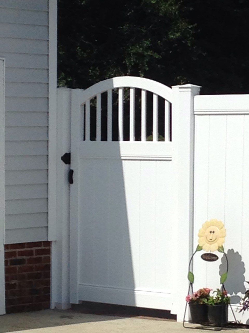 White gate with arched top, part of a white fence. A sunflower decoration stands nearby.