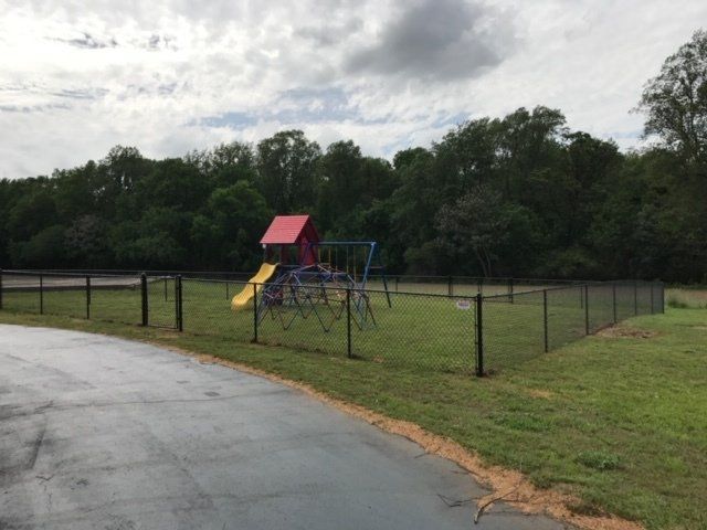 Playground behind a black fence, with a slide and climbing structure; green grass and cloudy sky.