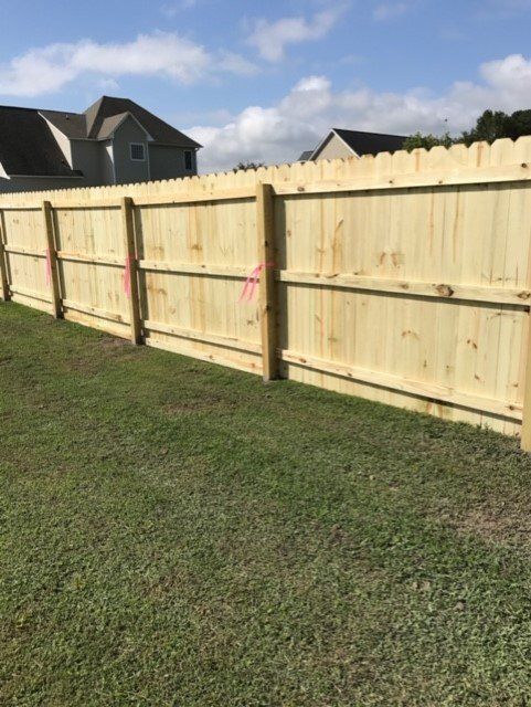 Wooden fence in a grassy yard, with a light blue sky and houses in the background.