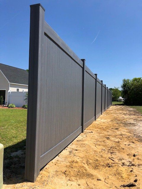 Gray vinyl privacy fence along a dirt path, under a blue sky.