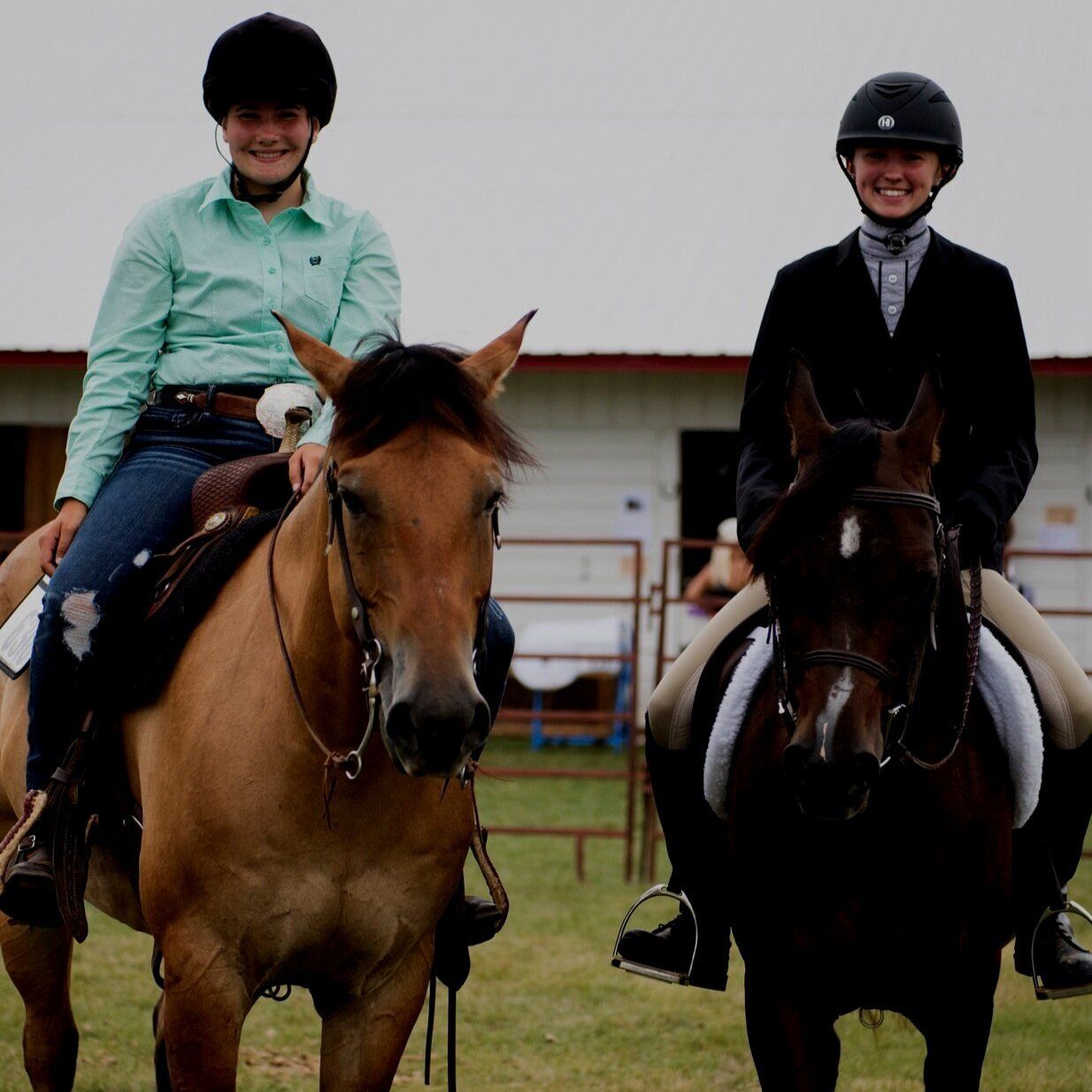 Two riders on horses, one in western attire, the other in English riding clothes, smiling outdoors.
