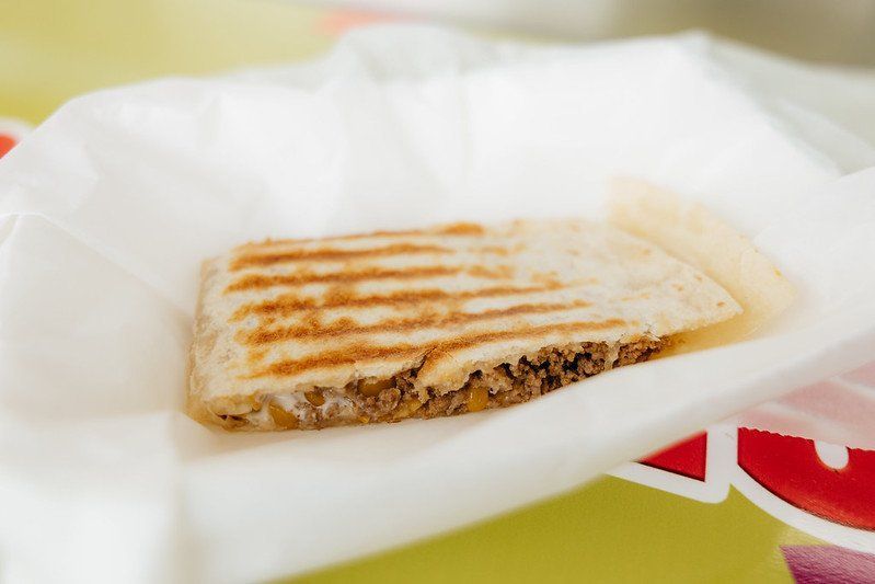 Grilled sandwich on white paper, showing grill marks and filling.