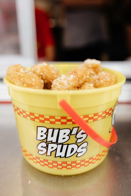 Yellow bucket of Bub's Spuds, filled with sugared fried potatoes. Red handle, checkered border.