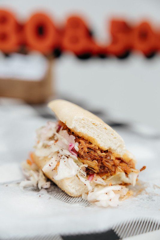 Pulled pork sandwich with coleslaw on a checkered tablecloth, orange 'BOO' in background.