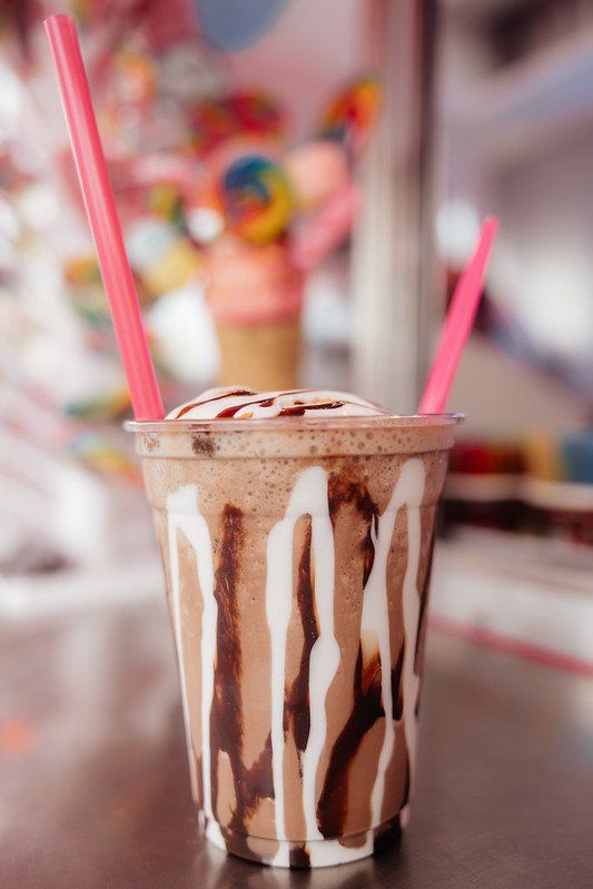 Chocolate milkshake with drizzles and pink straws, in front of a candy display.
