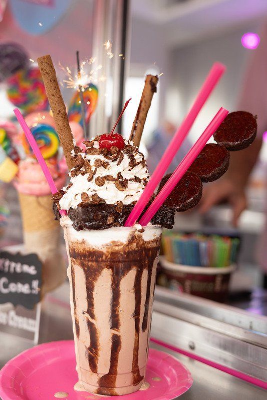 Chocolate milkshake with whipped cream, brownies, cookies, straws, and sparkler, on a pink plate.