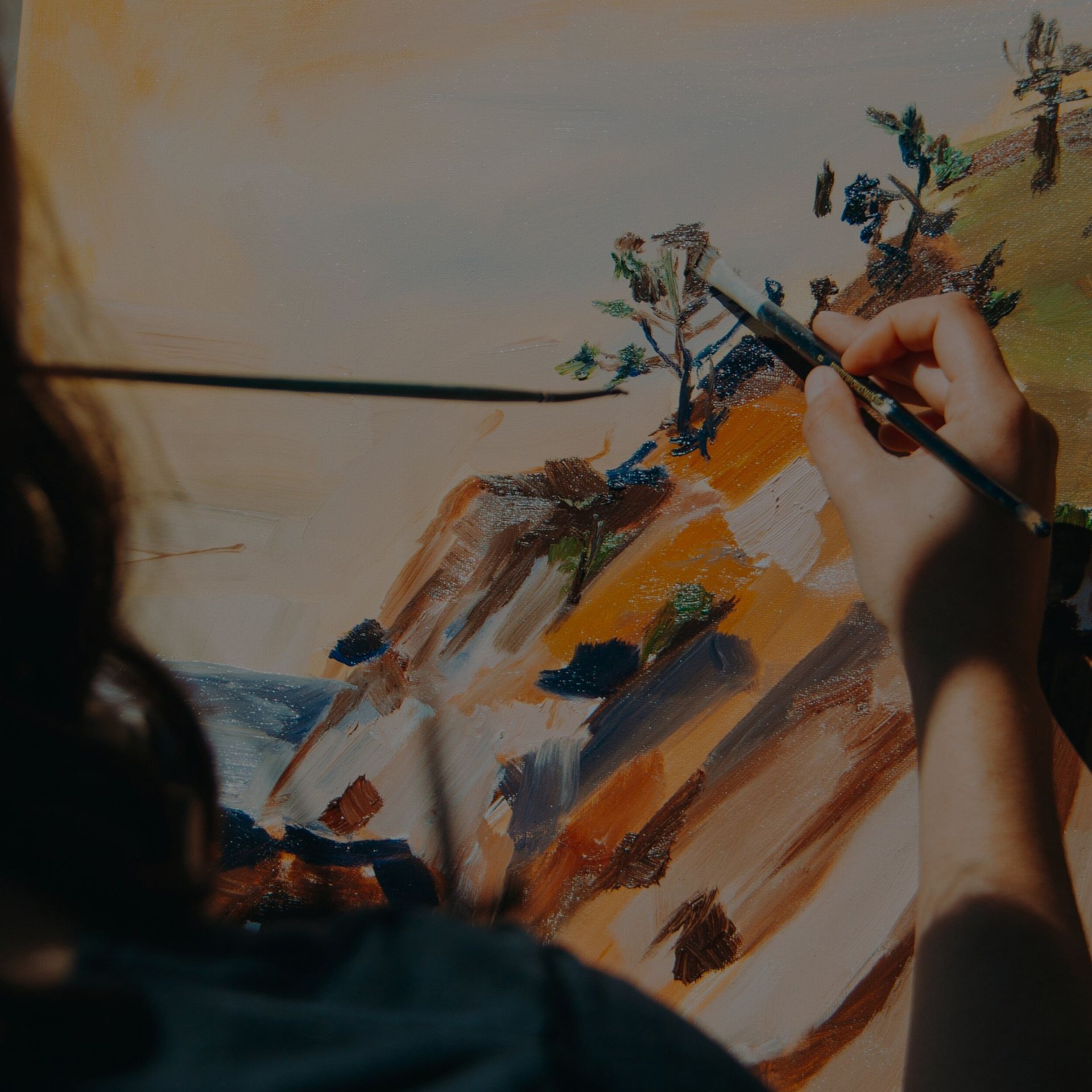 Person painting a landscape with brushstrokes on canvas; shades of brown, green, and blue.