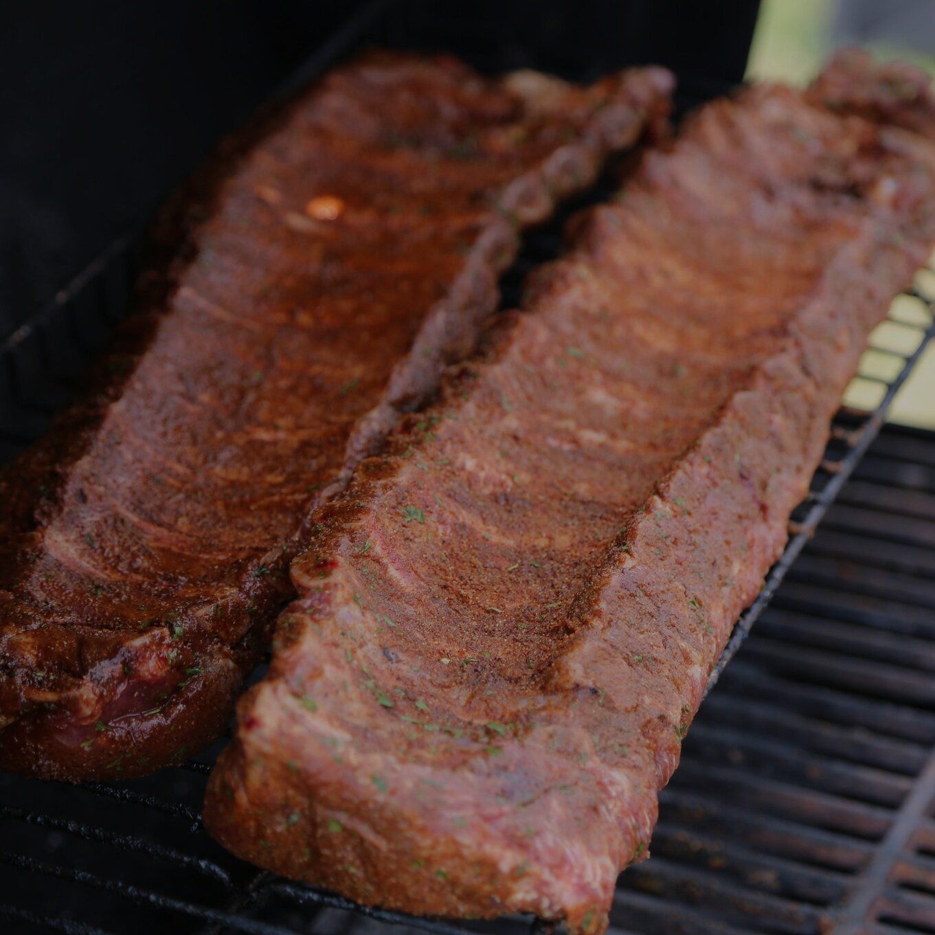 Two racks of seasoned ribs on a grill, ready for cooking.