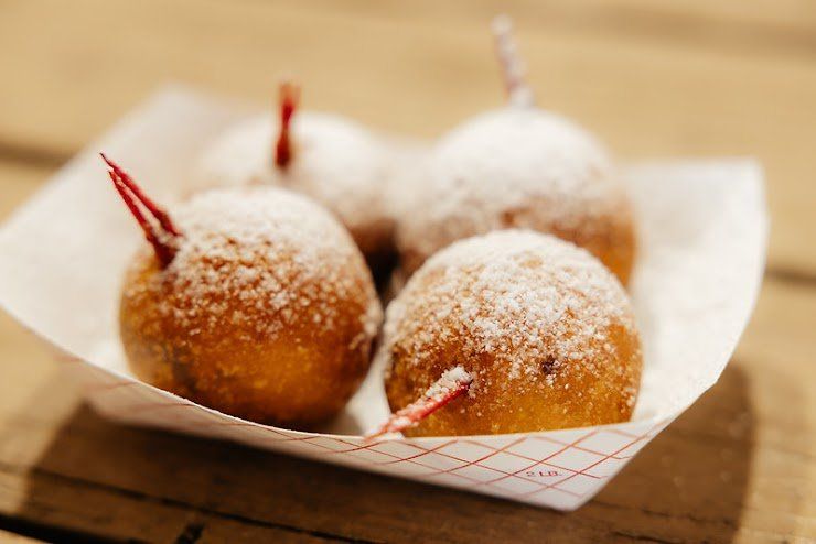 Fried dough balls dusted with powdered sugar, skewered with toothpicks, served in a paper tray.
