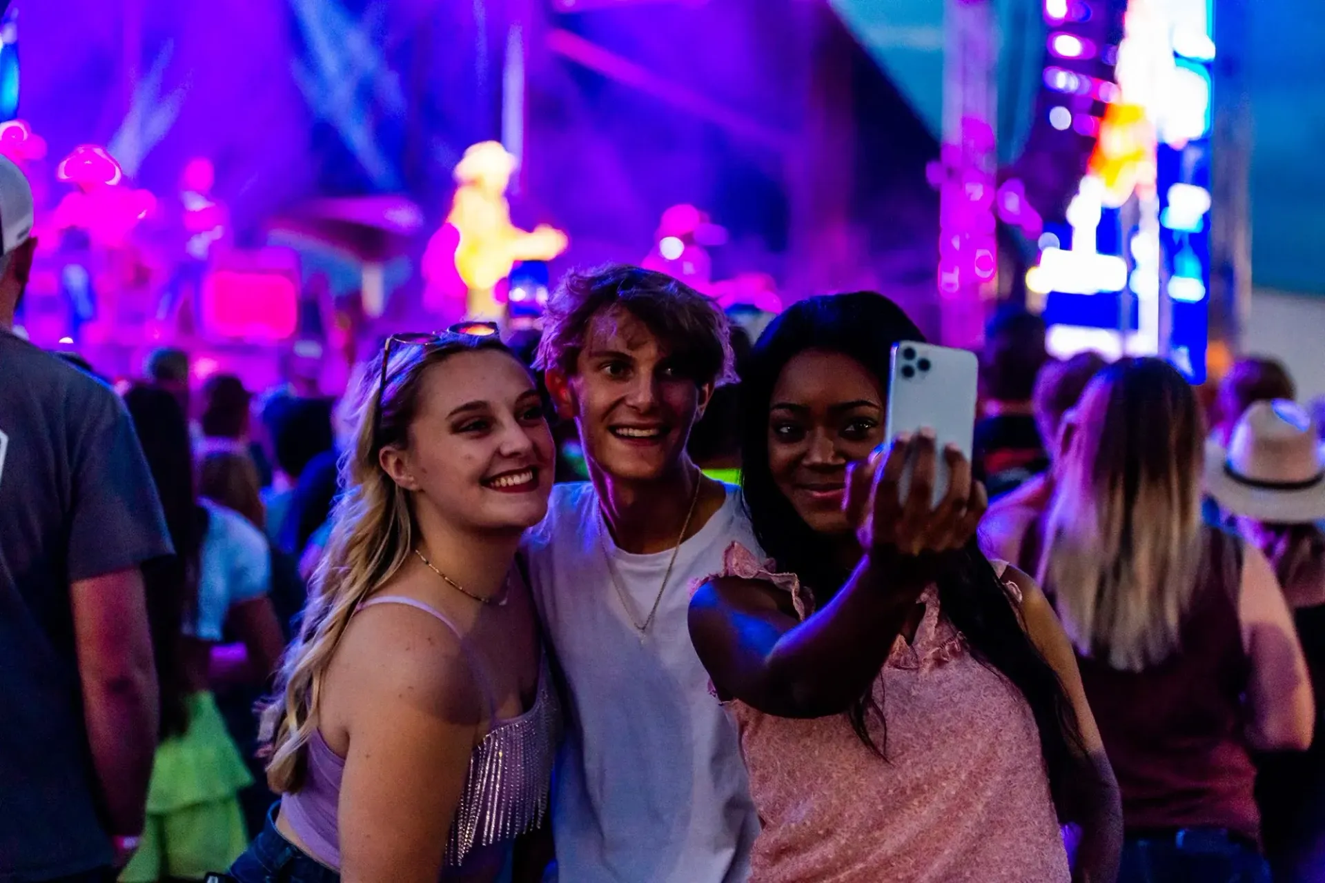 Three people taking a selfie at an outdoor event with stage lights; they are smiling.