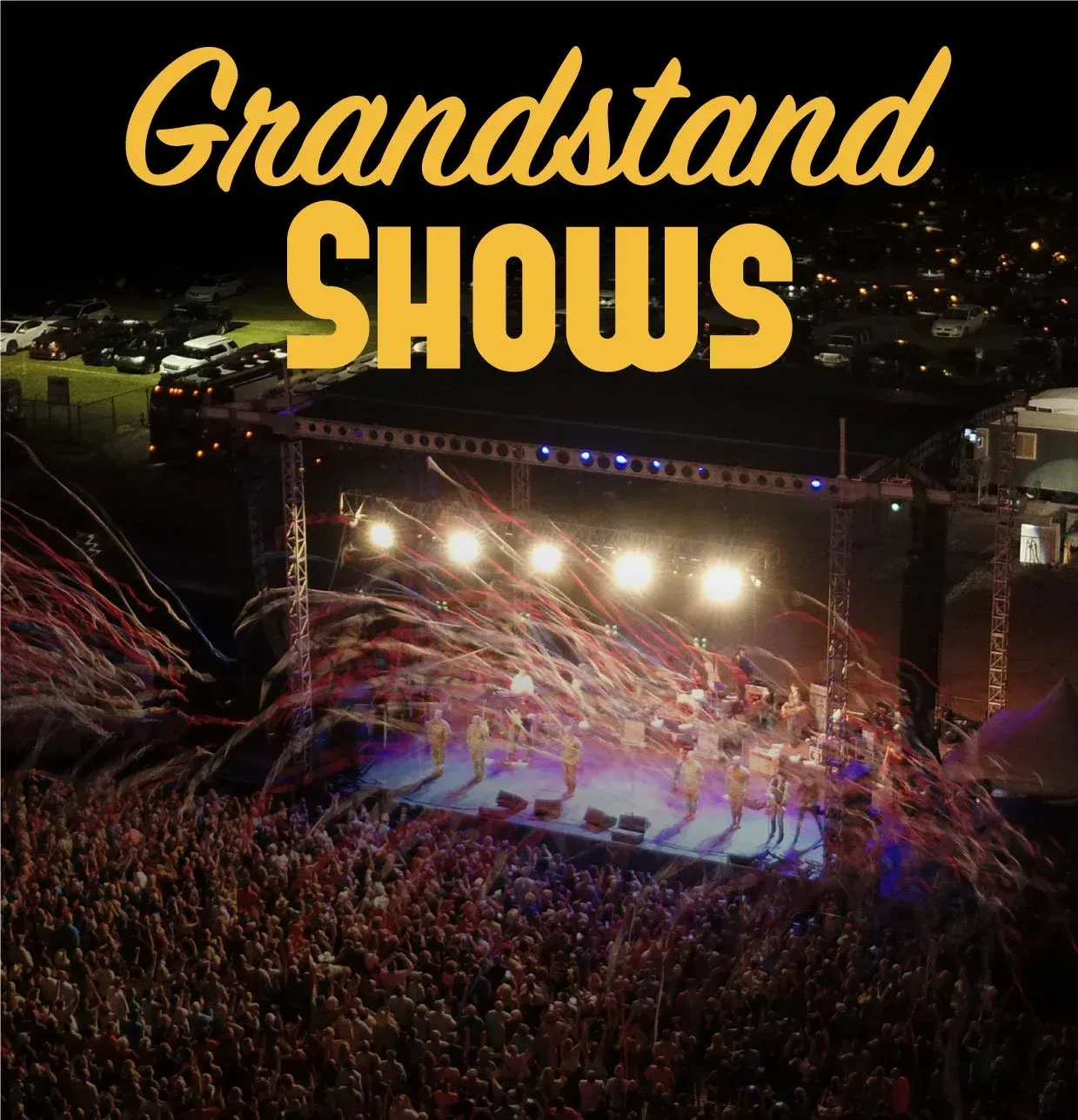 Grandstand show with a band on stage, confetti, and a crowd. Nighttime setting with spotlights.