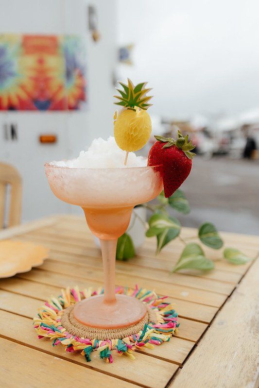 A colorful margarita cocktail with pineapple and strawberry garnish, on a wooden table.