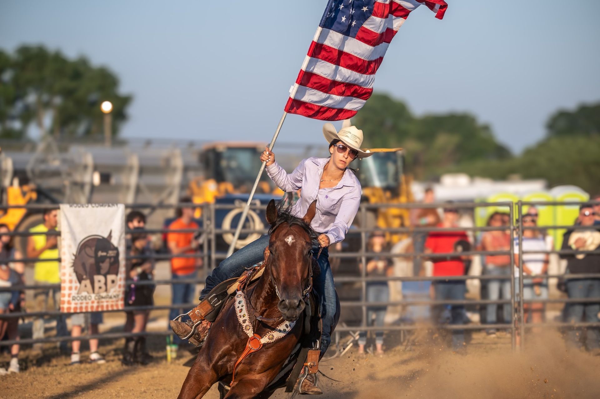 Woman on horse waves American flag at rodeo.
