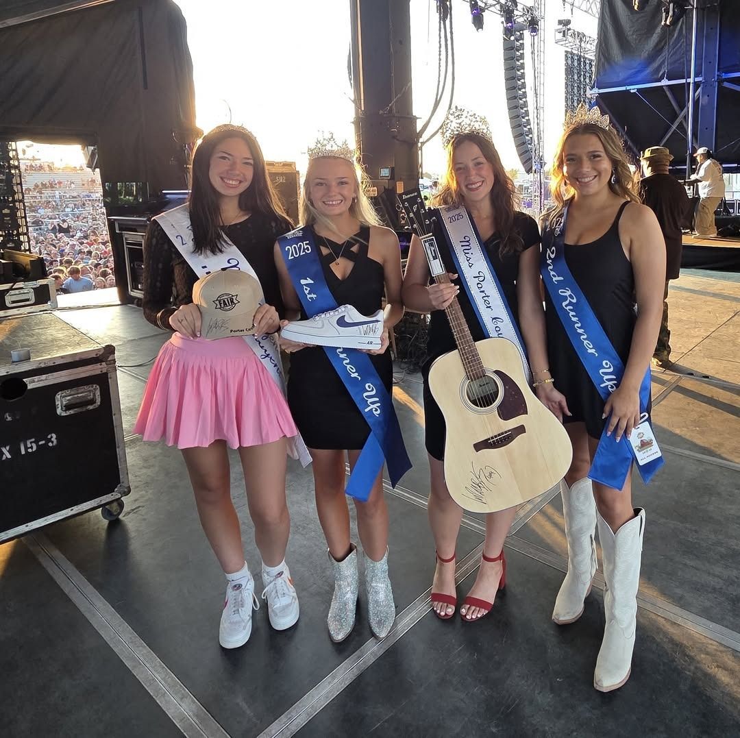 Four women in crowns and sashes pose with a tennis shoe, guitar, and trophy at a stage.