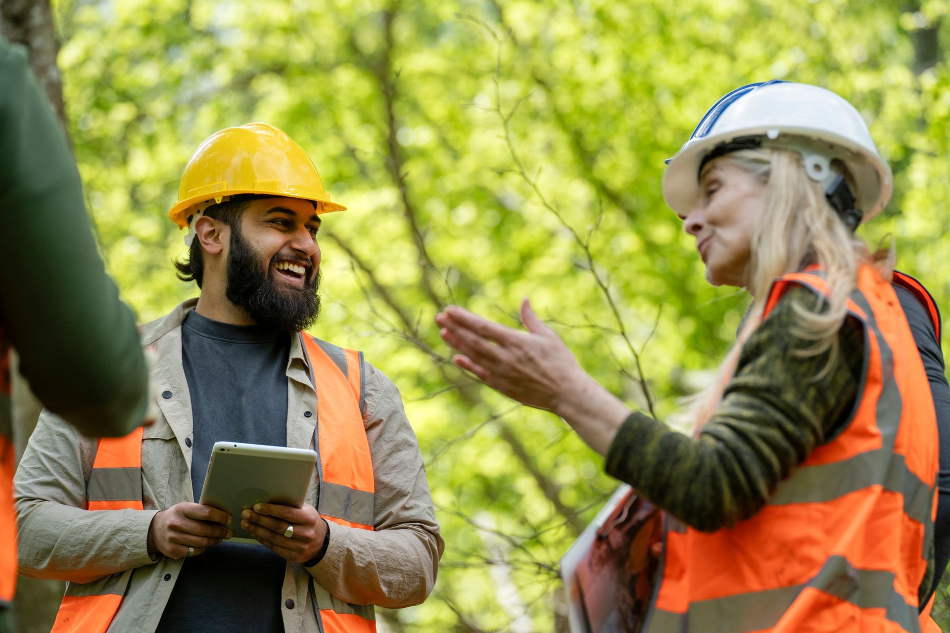 A group of construction workers are standing in a forest talking to each other.