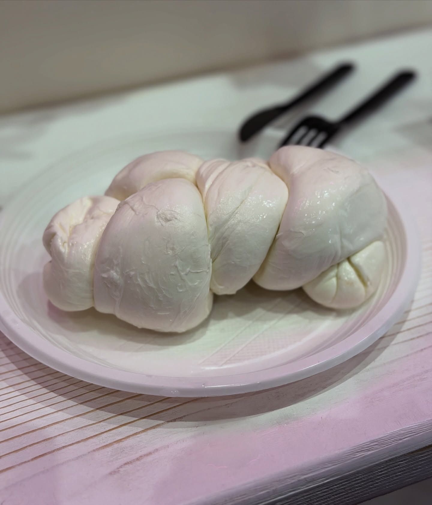 Formaggio bianco intrecciato su un piatto bianco con forchetta e cucchiaio neri.