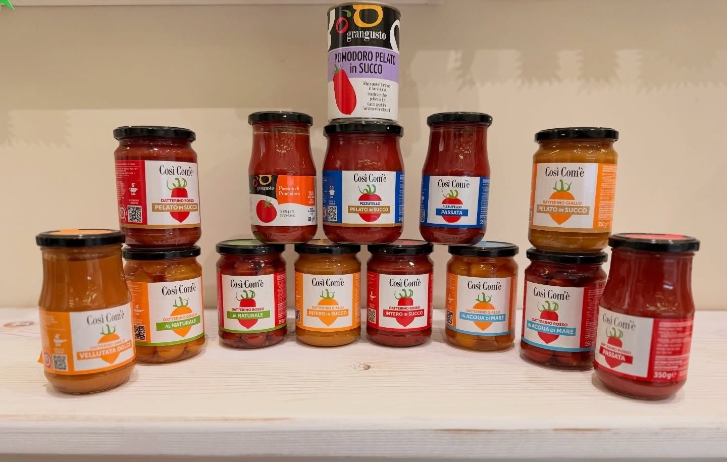 Assortimento di barattoli con etichette colorate su uno scaffale; alcuni sono impilati. I barattoli sembrano contenere salse o conserve.