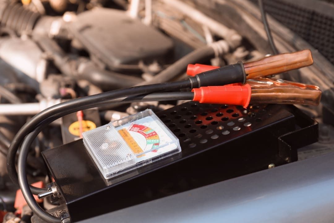 Jumper cables with red/black clamps, resting on a black box, in a car engine bay.